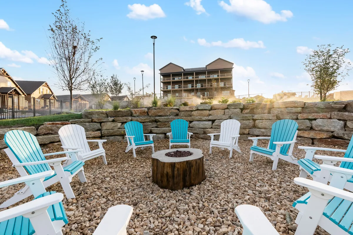 A cozy exterior scene centered around a fire pit, with Adirondack chairs arranged for gathering. The stone wall and sunset lighting create a welcoming, communal space ideal for storytelling and making s’mores.