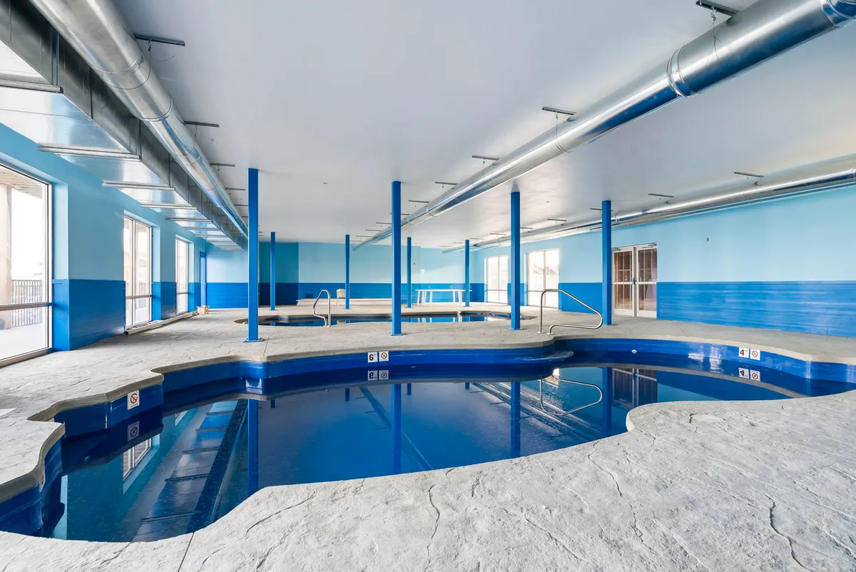 An inviting indoor pool with blue walls, large windows letting in sunlight, and a sleek, modern feel. The space feels refreshing, ideal for year-round swimming and relaxation regardless of the weather.