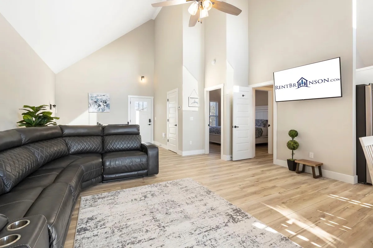 A spacious lower-level living area featuring a large sectional sofa, a wall-mounted TV, a decorative rug, and a touch of greenery in the corner. The space feels cozy and is ideal for lounging, watching movies, or quiet relaxation.