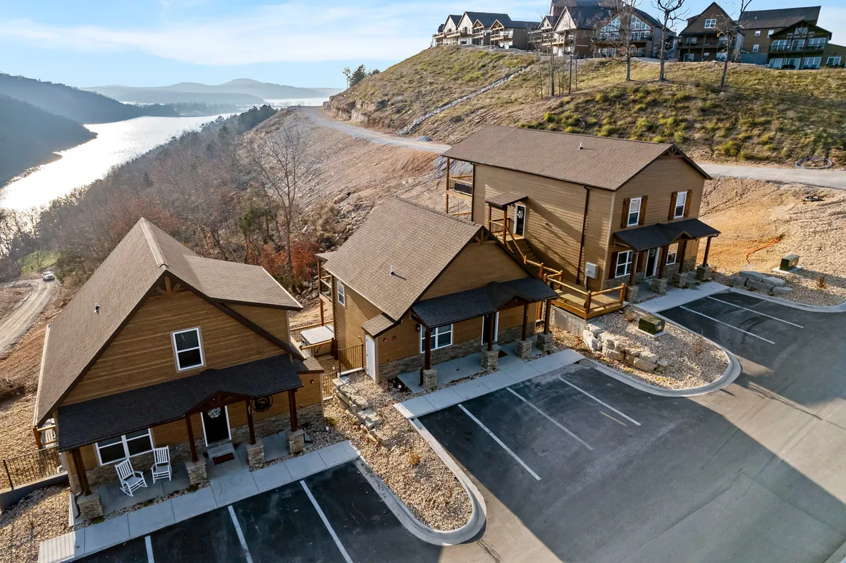 A peaceful exterior view of wooden cabins overlooking a lake and hillside, with porches ideal for relaxing after a walk in nature. The serene surroundings invite exploration and are an appealing setting for walks with dogs.