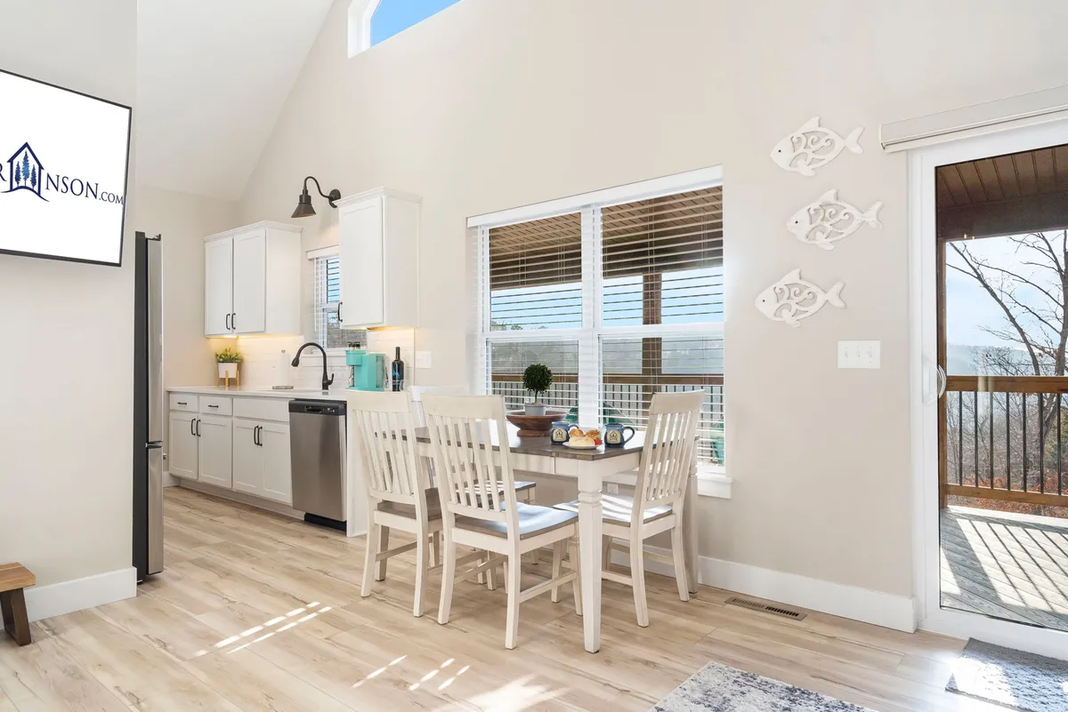 A bright kitchen and dining space featuring a modern kitchen area, a spacious dining table, and large windows adorned with decorative fish ornaments. The room is filled with natural light and offers inviting views of the surrounding nature, making it ideal for cooking, dining, and socializing.