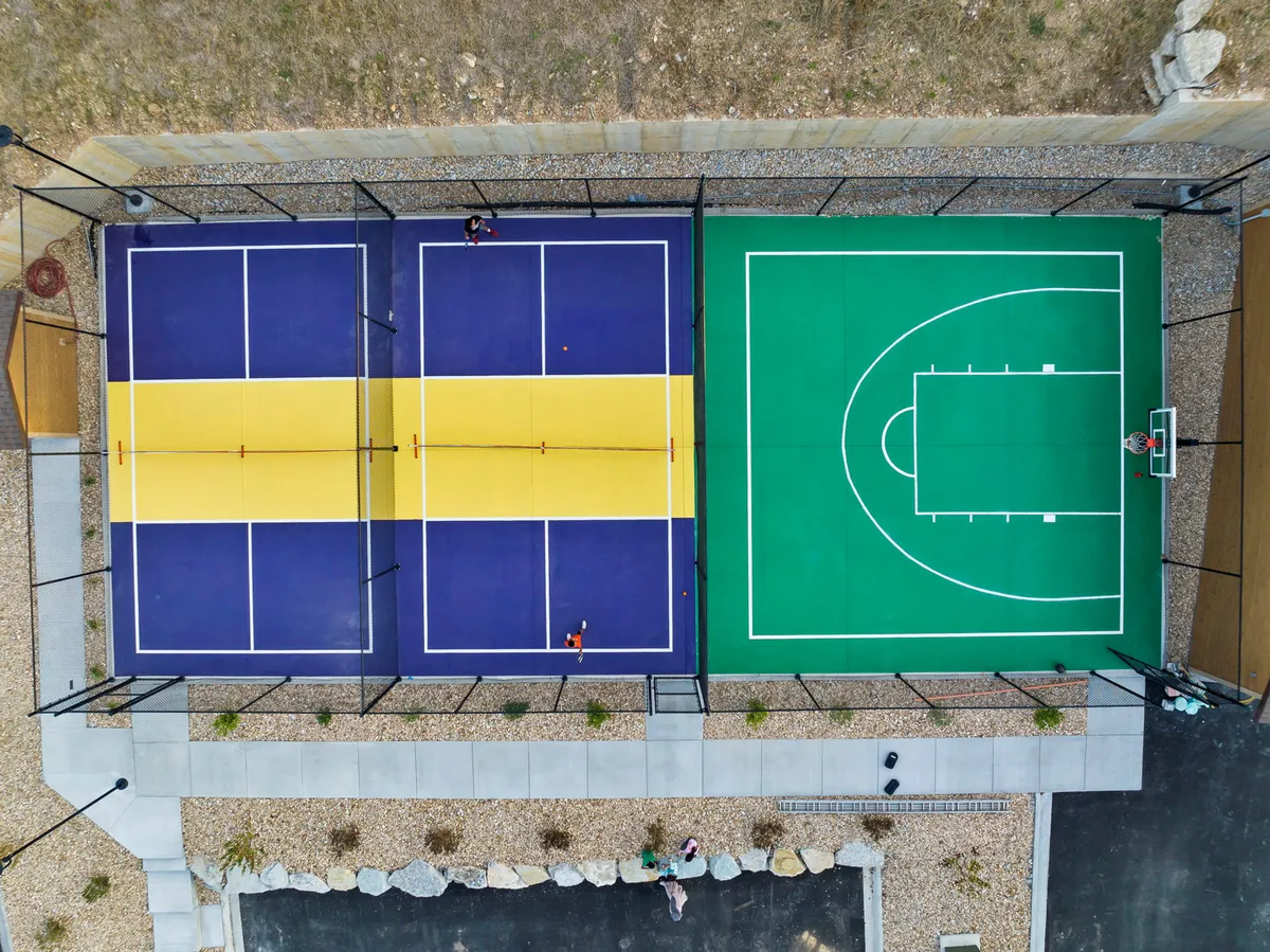 The exterior scene showcases resort-style tennis and basketball courts with players engaged in friendly competition. Lush landscaping surrounds the courts, highlighting the vibrant, active resort atmosphere.