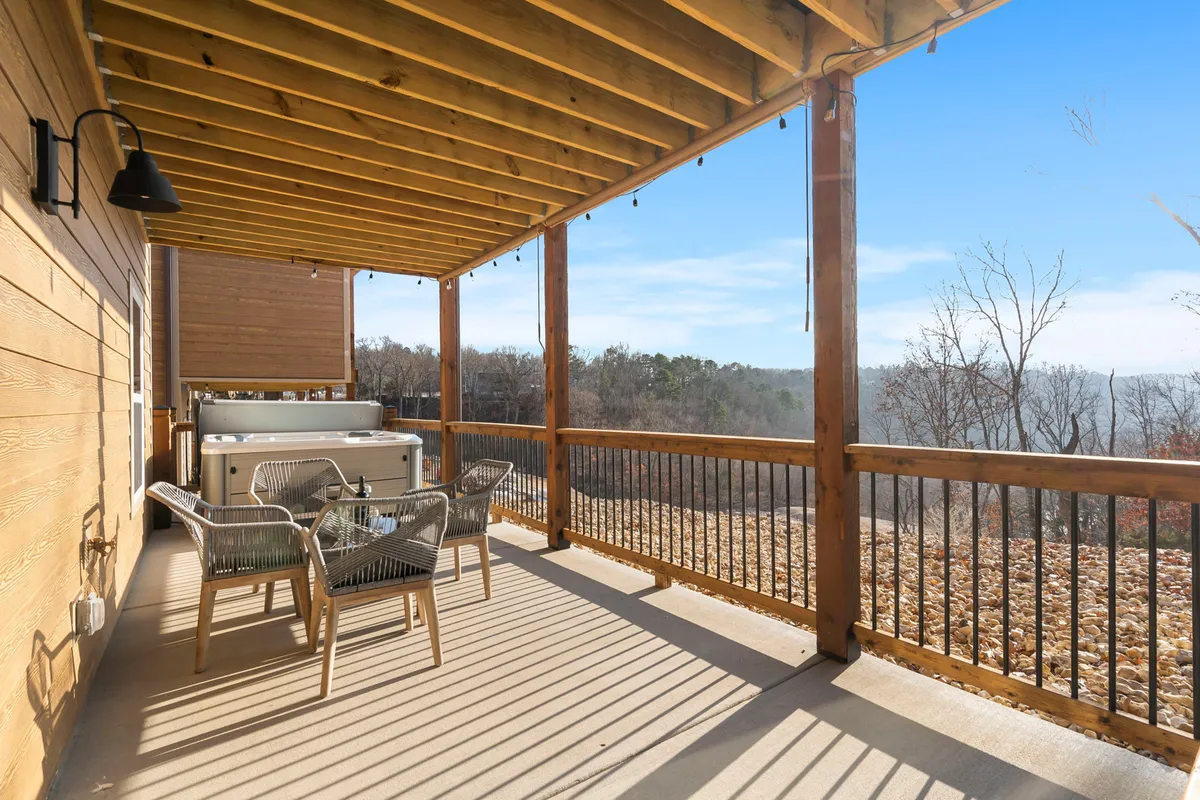 A spacious deck features an outdoor hot tub and seating area overlooking a scenic landscape. The inviting hot tub is ideal for evening relaxation, while the comfortable chairs create a welcoming environment for conversation and shared moments under the open sky.