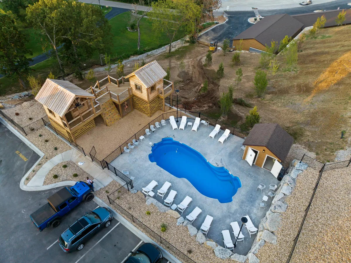 A lively exterior scene featuring a sparkling swimming pool, comfortable lounge chairs, and a vibrant play structure nearby. Children are seen playing while adults relax, with beautifully landscaped surroundings that enhance the atmosphere.