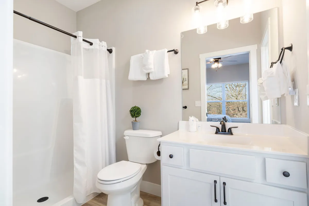 A bright, inviting bathroom with a modern vanity, sink, toilet, shower area, large mirror, and a decorative plant. The space feels fresh and serene, ideal for self-care and unwinding.