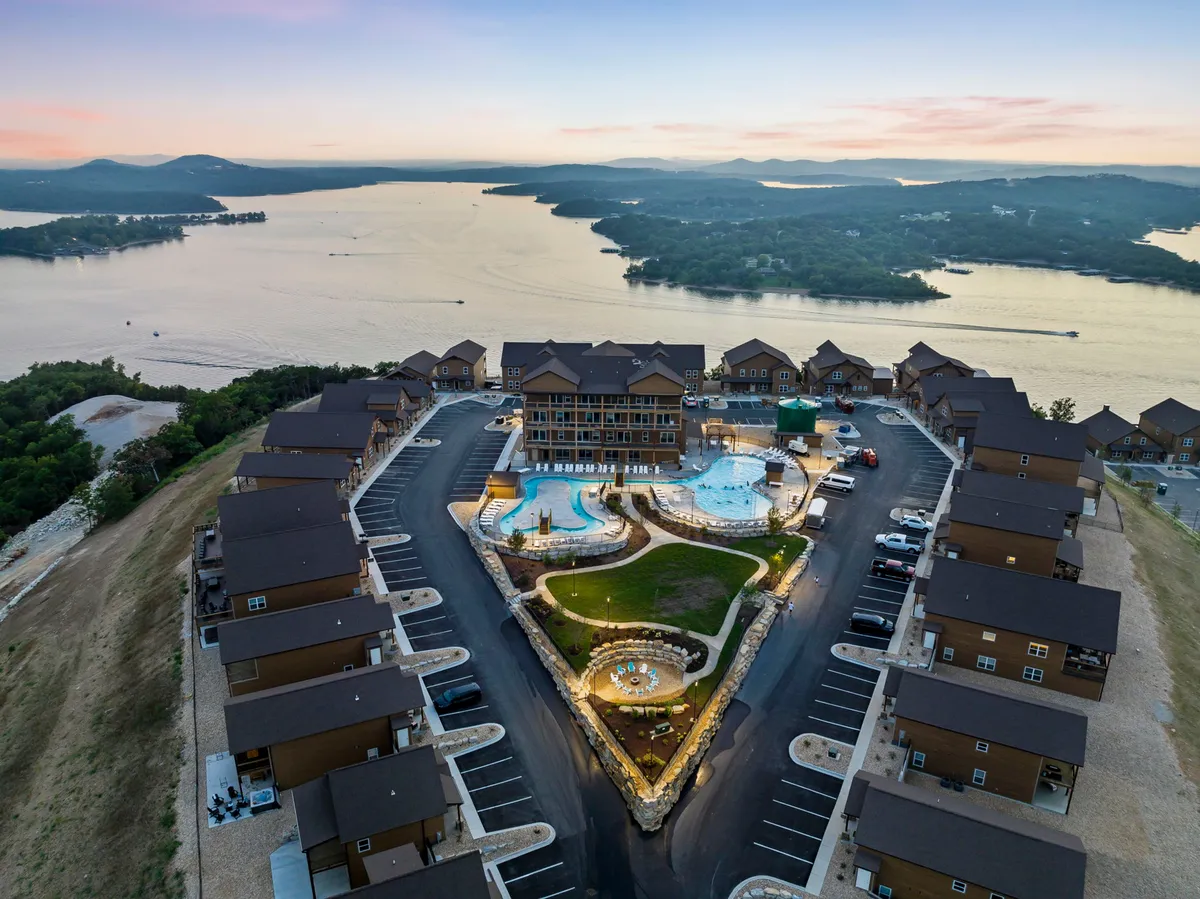 This image features a resort-style outdoor pool with landscaped gardens, a lake view, and elegant building architecture. People can be seen swimming, sunbathing, and gathering for social activities, evoking a relaxed, vibrant, and communal atmosphere ideal for families.