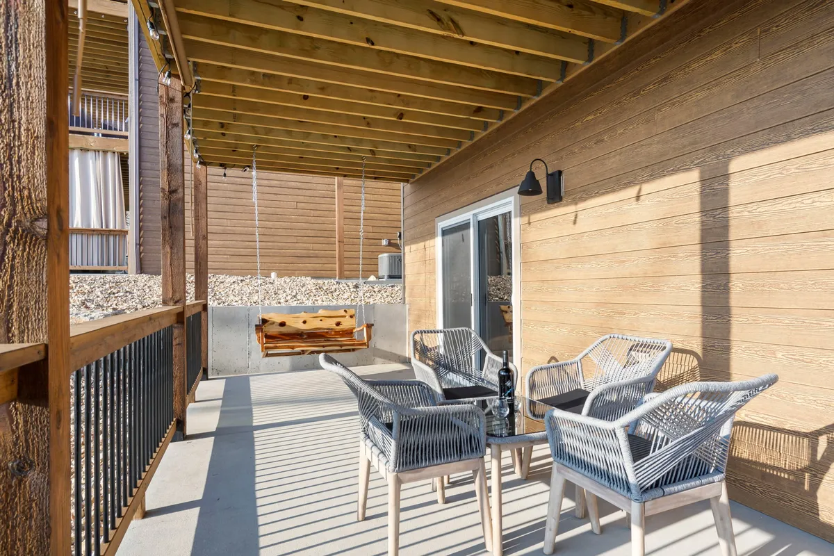 This exterior image features an inviting outdoor seating area with a swing bench and a glass table, surrounded by lush greenery. The space has a relaxed, casual vibe that suggests an ideal spot for unwinding after outdoor adventures with a pet.